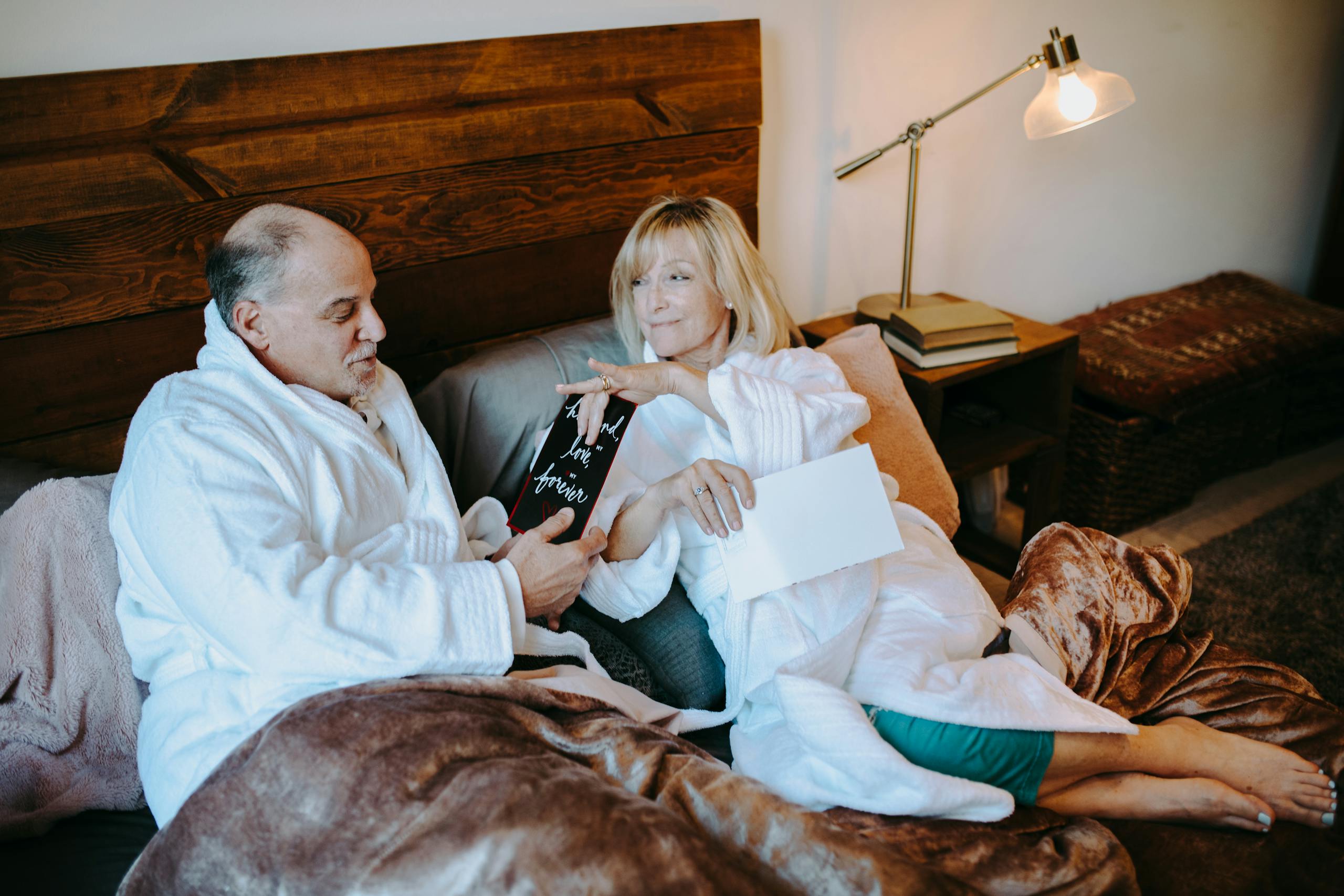 Senior couple exchanging gifts in a warm, intimate bedroom setting, celebrating an anniversary.